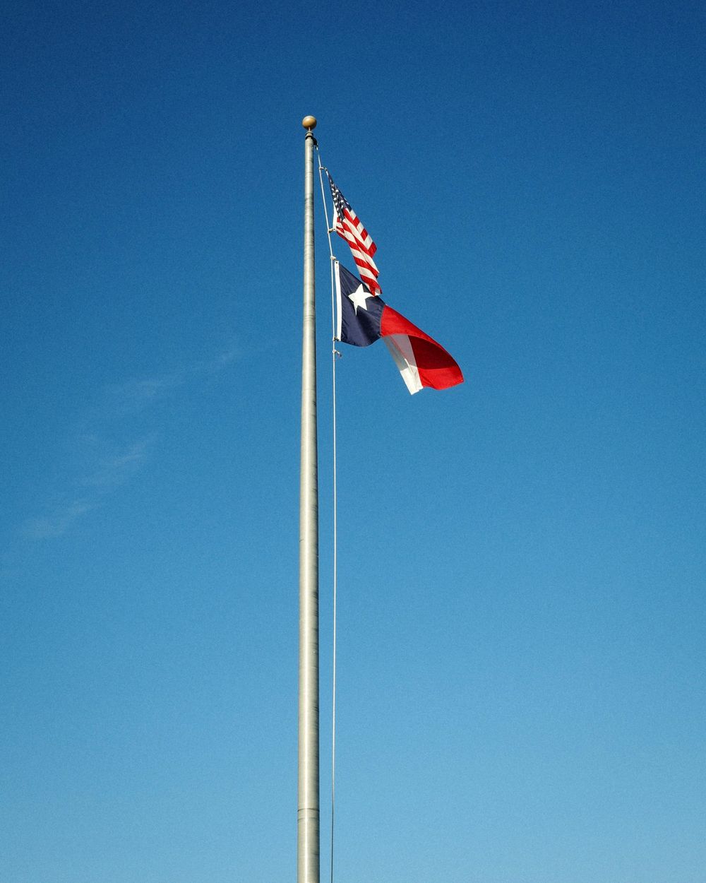 The United States and Texas flags flying against a clear blue sky